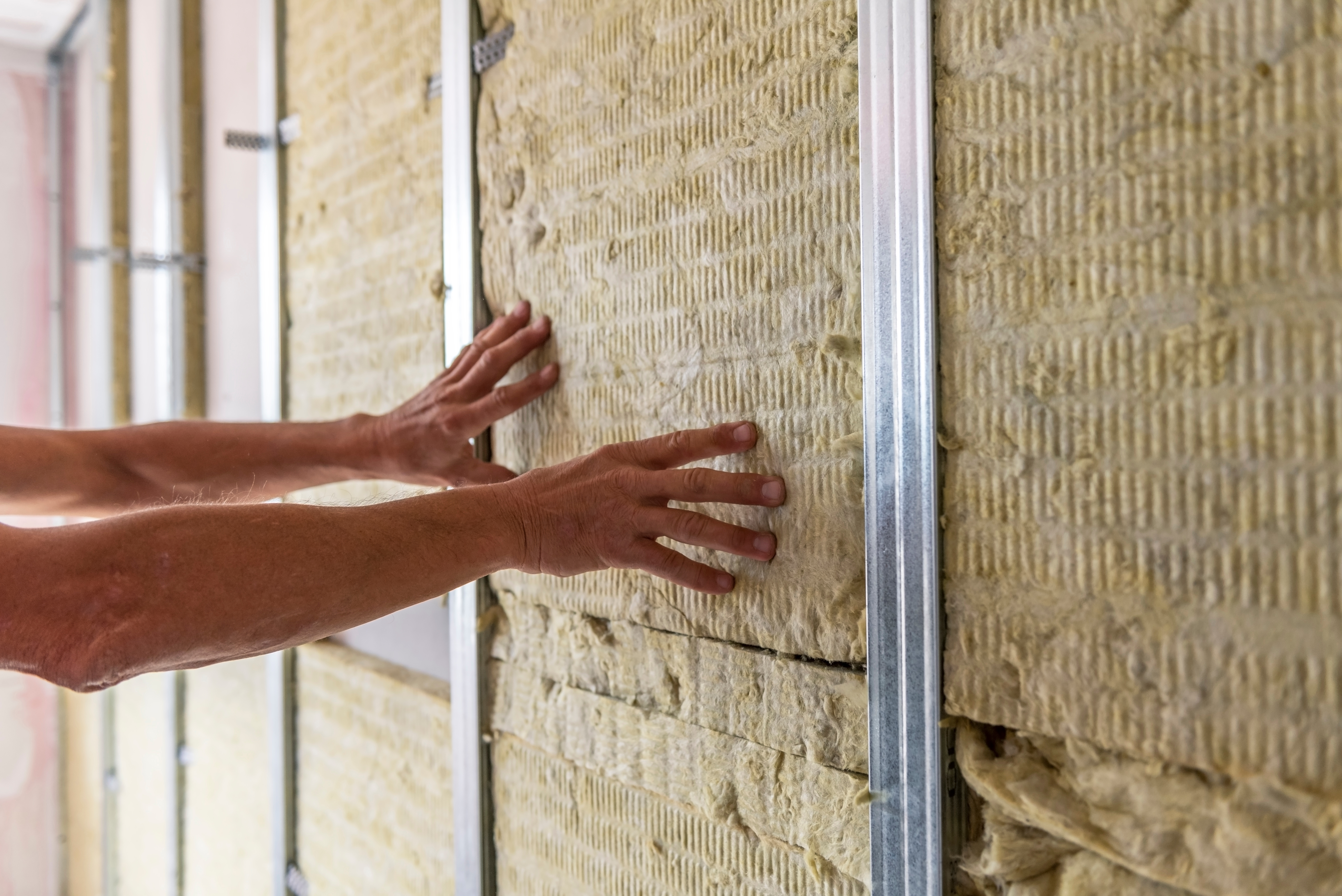 Werknemer die de muur van een kamer isoleert met minerale wol voor thermische isolatie