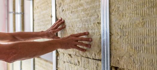 Een man raakt de muur van een geïsoleerde kamer aan om het belang van isolatie in huis te illustreren.