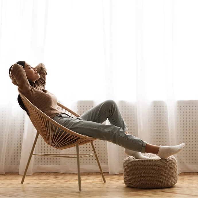 La femme est une jeune femme décontractée, assise sur une chaise à la maison. La femme qui se sent heureuse et positive se réjouit de son bien-être et se détend près d'une fenêtre dans un appartement moderne et confortable.