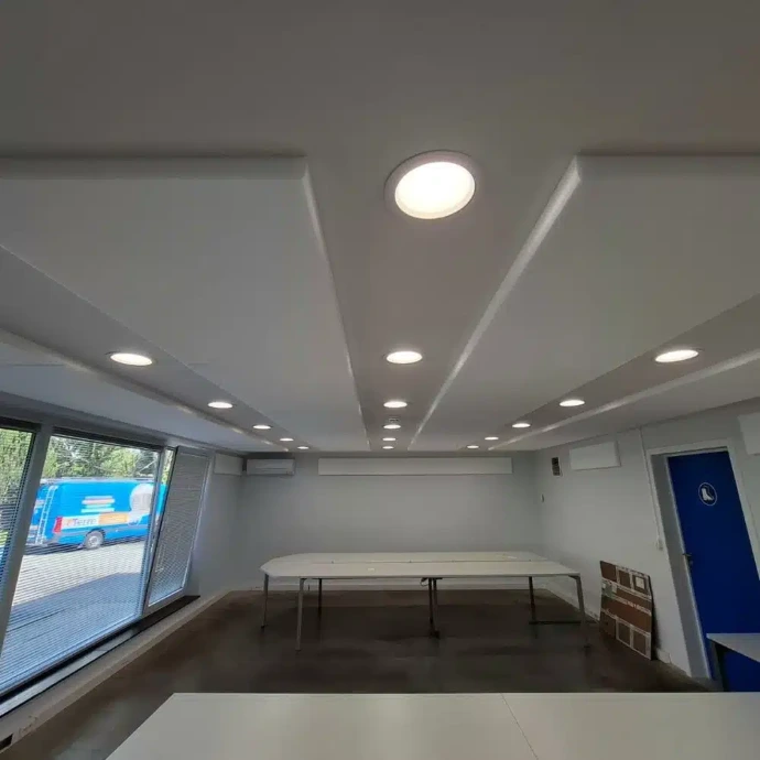 Salle de réunion lumineuse avec des tables au centre et des panneaux en mousse de mélamine au mur et au plafond