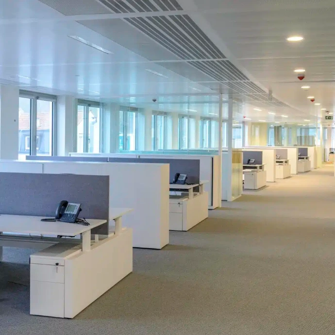 Vaste open space lumineux avec des bureaux blancs séparés par des panneaux acoustiques en feutre