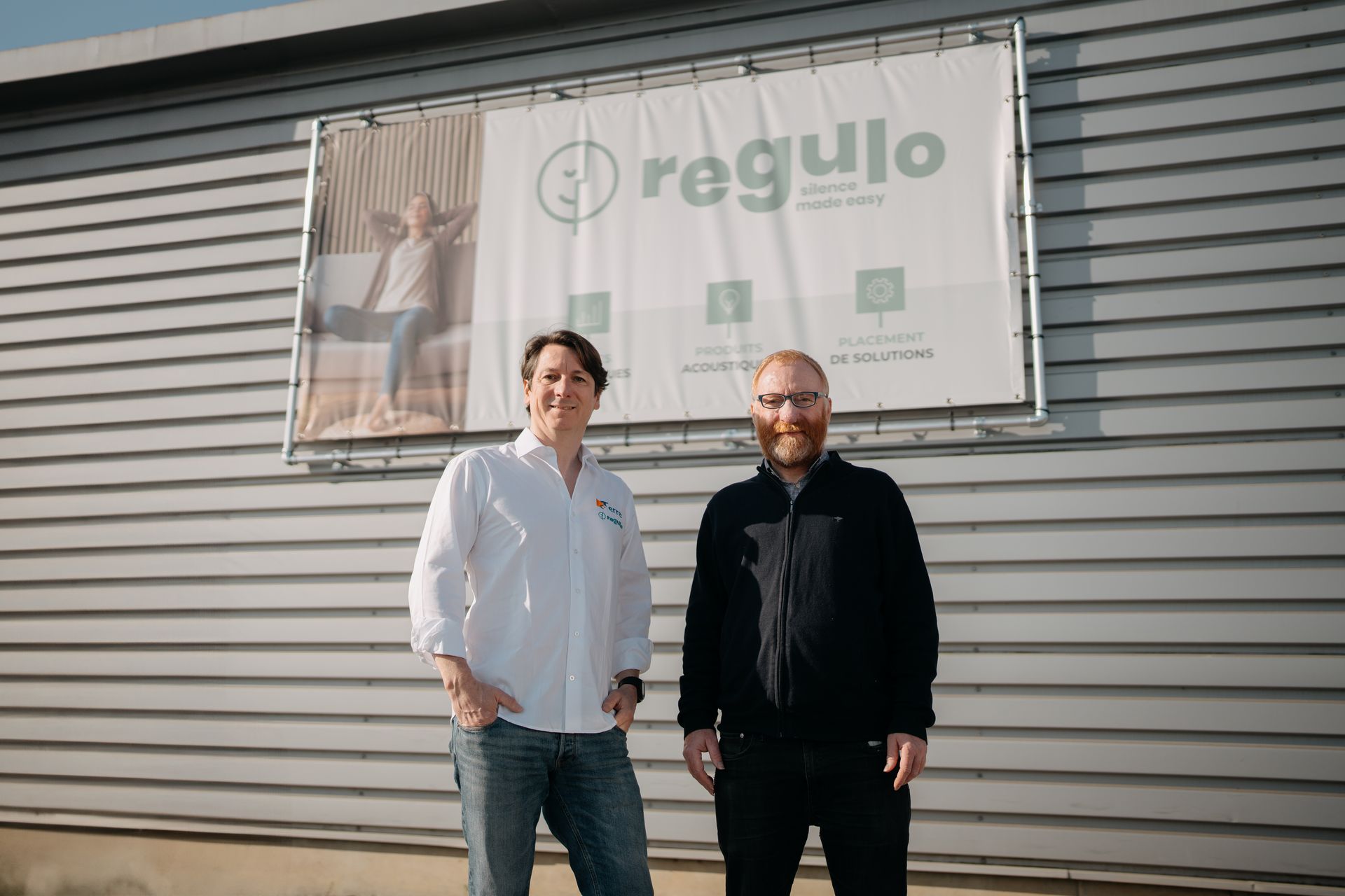 Deux hommes posent devant une affiche